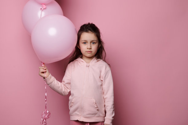 小女孩拿着一束粉色粉彩气球，看着相机，孤立的粉红色背景与复制广告空间图片下载