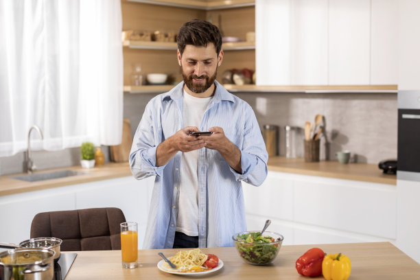 微笑的成年白人男子在休闲做饭，用智能手机拍意大利面图片下载