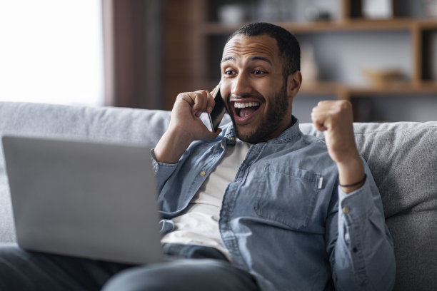 喜讯：黑人男子在家用手机和笔记本电脑庆祝成功图片下载