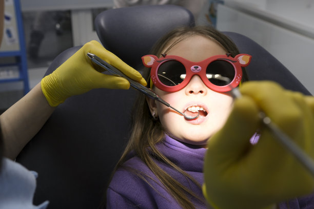 小儿牙科特写小女孩张开嘴露出牙齿医生看她是否有龋齿填充物治疗由医生检查眼睛发亮黄色的卫生手套图片下载