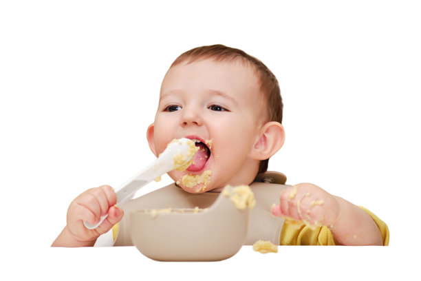 快乐的学步男孩学会了自己用勺子喝粥，坐在儿童椅上，孤立在白色背景上。一岁的孩子，微笑着用手和勺子吃饭图片下载