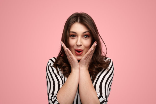 惊讶的年轻女士大叫和触摸脸颊对粉红色的背景图片下载
