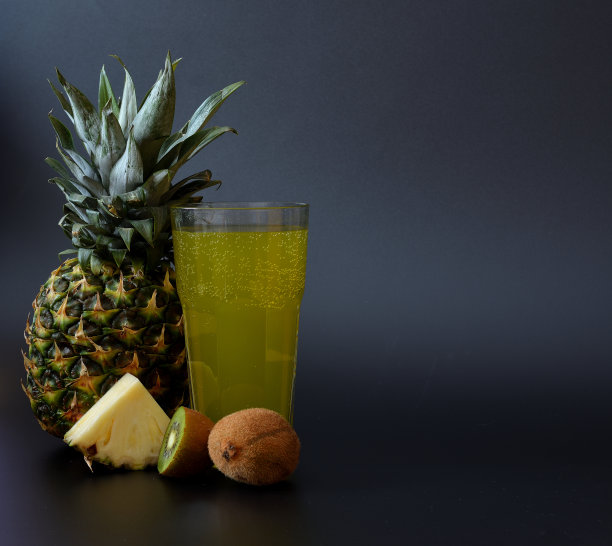 一个高脚杯，黑色背景是热带水果的混合物，旁边是成熟的菠萝和猕猴桃。图片下载