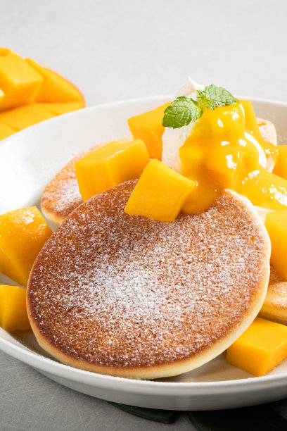 美味的日式蛋奶酥煎饼，灰色的桌子背景上有芒果和果酱。图片下载