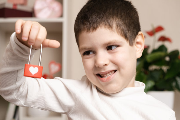 一个5岁的可爱男孩用他的心拿着一把锁，微笑着。情人节和孩子，初恋，学龄前儿童图片下载