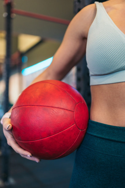 垂直裁剪的年轻女运动员在健身房抱着一个药球或大满贯球在她的手臂下的图像。图片下载
