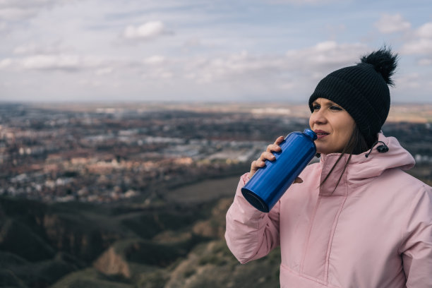 年轻的女徒步旅行者在羊毛衬里和羊毛帽休息喝水和补充水分在山顶。图片下载