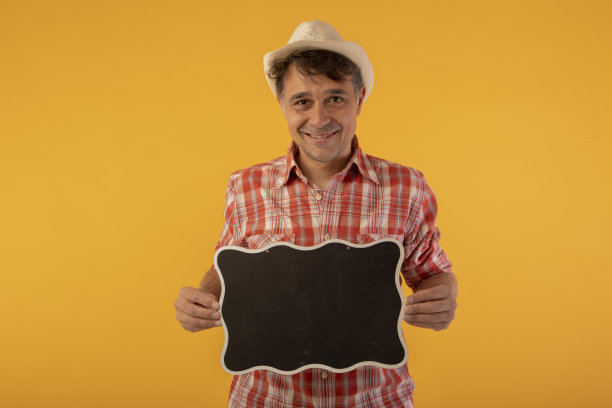 黑发男子，戴着帽子，穿着彩色衬衫，面带微笑，手里拿着一块黑色的牌子图片下载