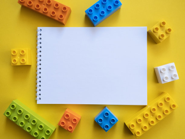 螺旋记事本在黄色背景周围的塑料积木，俯视图。学校或学前教育背景。为你的文字建立空的塑料块。图片下载