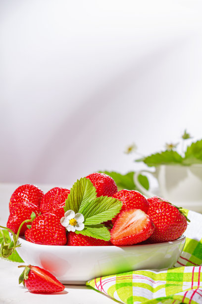草莓放在桌上的白瓷碗里。一碗多汁的新鲜成熟的红草莓图片下载