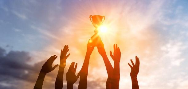 剪影商业团队手持获奖奖杯展示胜利商业成功夕阳背景。胜利的队伍捧着奖杯，迎着灿烂的阳光。男子手持奖杯图片下载