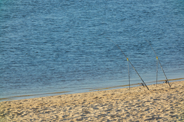 在一个阳光灿烂的日子里，两根钓鱼竿被放在沙滩上图片下载