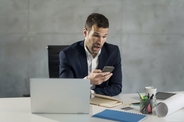 惊讶的商人在办公室打电话。图片下载