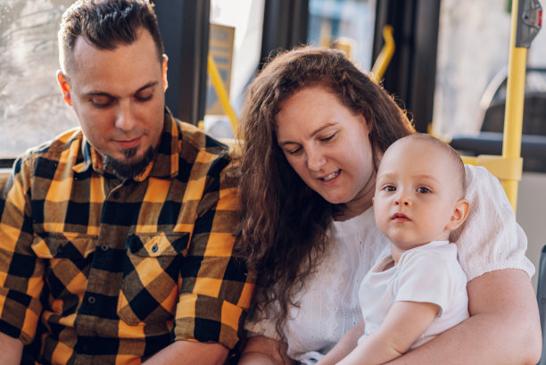 快乐的父母和儿子坐在公共汽车上，婴儿坐在母亲的大腿上。图片下载