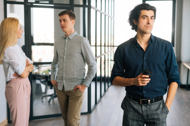 自信的创业企业家的肖像，穿着休闲装，手里拿着外卖咖啡杯，站在办公室，看着相机。图片下载