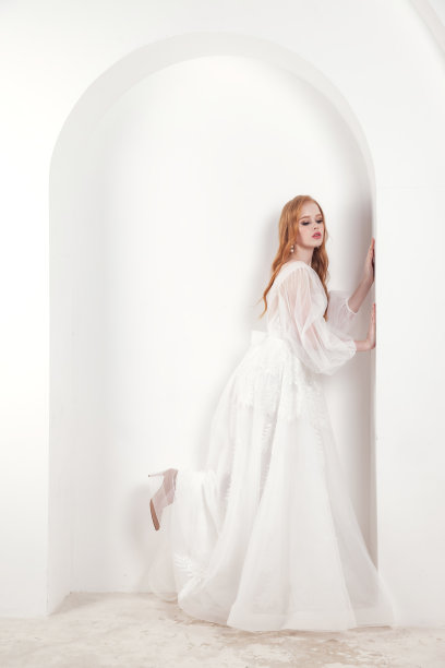 全长时尚新娘爱尔兰红发女士在白色婚纱摆姿势在白色背景。时髦漂亮的女人站在墙上。时尚潮流风格美概念。复制广告文字空间图片下载