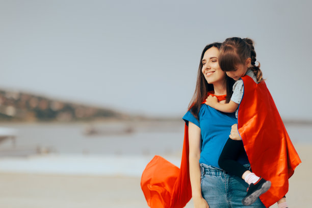 快乐的超级妈妈抱着穿着斗篷的女儿图片下载