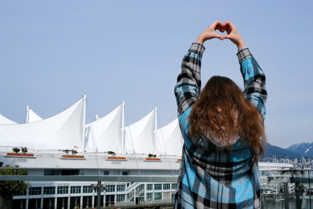 少女背对镜头用手比心，加拿大广场停靠着海洋光辉号游轮图片下载