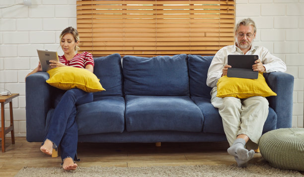 小玩意上瘾。父亲和女儿坐在家里客厅的沙发上，手里拿着不同的电子设备。图片下载