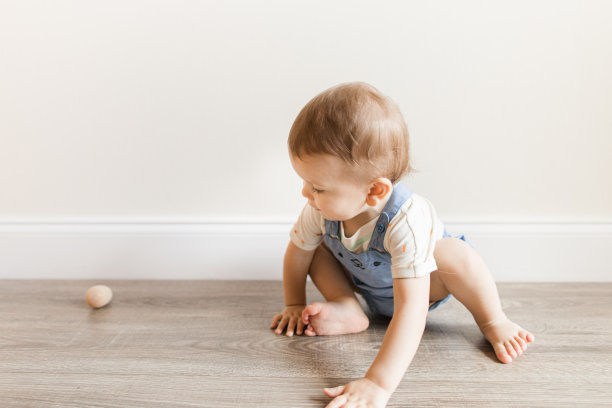 一个15个月大的古巴裔美国男婴，浅棕色短发，棕色眼睛和12只脚趾，穿着胡萝卜连体衣和蓝色兔子工作服，还有蓬松的兔子尾巴，光着脚坐在家里的地板上玩木制鸡蛋玩具图片下载