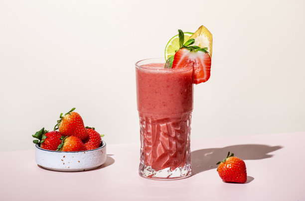 鹈鹕夏季无酒精鸡尾酒或鸡尾酒，草莓，香蕉，糖浆，桃子汁，柠檬和冰在高球杯。米色粉红色香草色背景，硬光，阴影图案图片下载