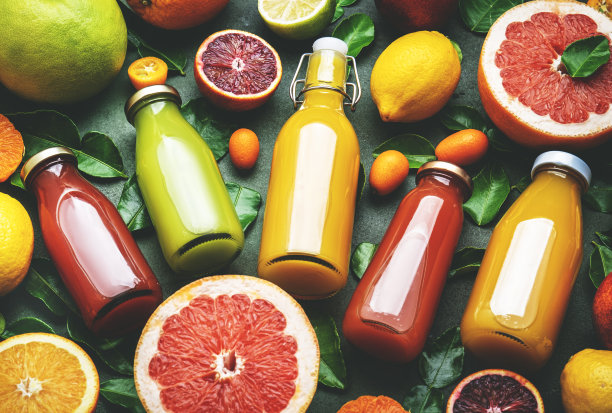 夏季饮料。柑橘果汁，新鲜和冰沙，食物背景，俯视图。混合不同的完整和切块的水果:橙子，葡萄柚，酸橙，带叶子的橘子和绿色桌子上的瓶装饮料图片下载