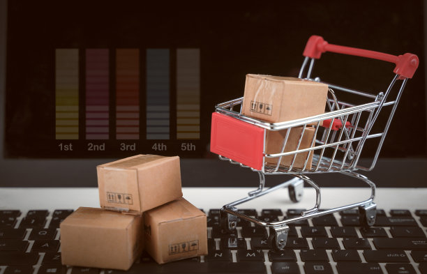 网上购物，送货上门。棕色纸盒在购物车与笔记本电脑键盘在桌子办公室。消费者只需指尖即可轻松购物。电子商务和客户体验概念。图片下载