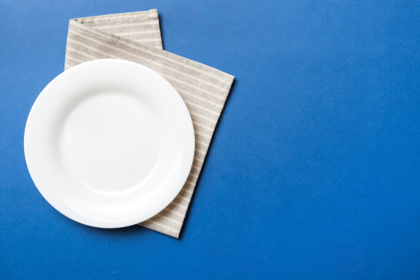 顶部视图上的彩色背景空圆形白色盘子在桌布上的食物。在餐巾纸上空出盘子，为你的设计留出空间图片下载
