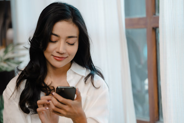 微笑的女孩用手机聊天信息或网上购物从家里在早上，快乐的年轻亚洲女人放松在家里舒适的沙发上发短信在智能手机上图片下载
