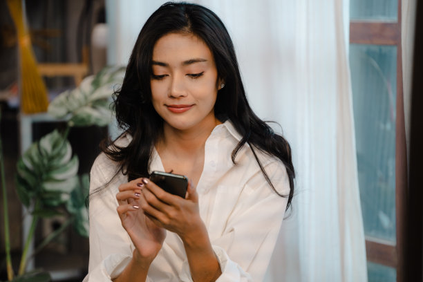 微笑的女孩用手机聊天信息或网上购物从家里在早上，快乐的年轻亚洲女人放松在家里舒适的沙发上发短信在智能手机上图片下载