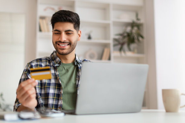 微笑的年轻人使用电脑和信用卡，选择性的关注图片下载