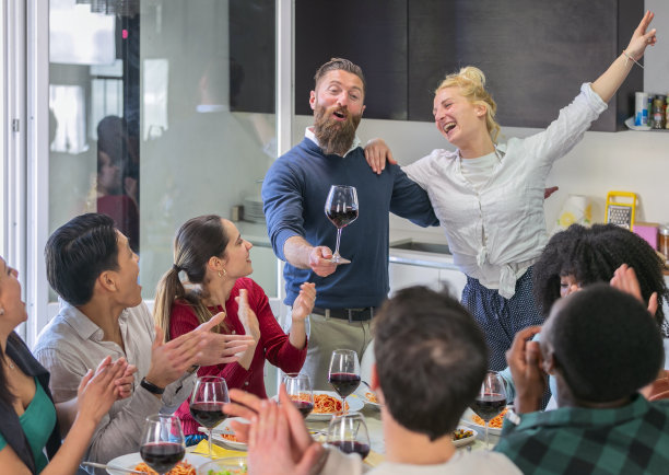 年轻的多民族朋友围坐在餐桌上，庆祝感恩节，在家共进晚餐，敬酒，敬酒，嘉宾端酒致词图片下载