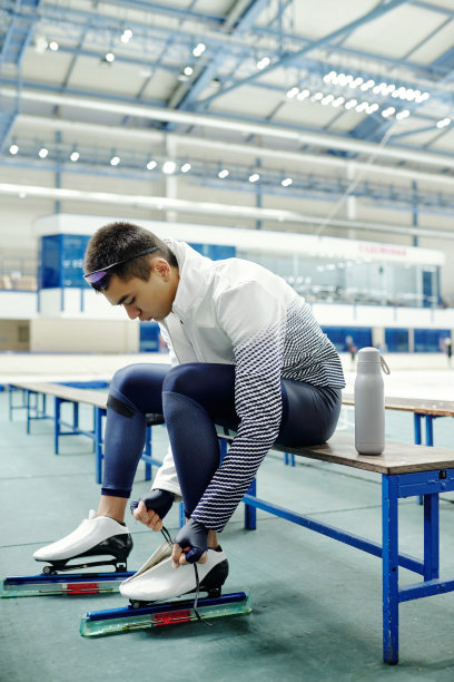 活跃的家伙在运动服弯曲向前，同时系鞋带的冰鞋图片下载