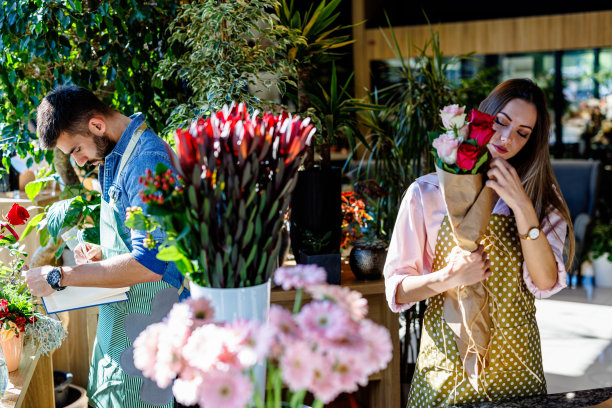 一对年轻的花匠正在花店里插花并分析。图片下载