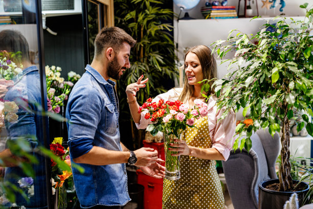 一位女花匠正在花店里卖花给一位年轻男子。图片下载