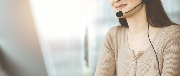 年轻的女孩戴着耳机，正坐在阳光明媚的办公室的桌子上与一家公司的客户交谈图片下载