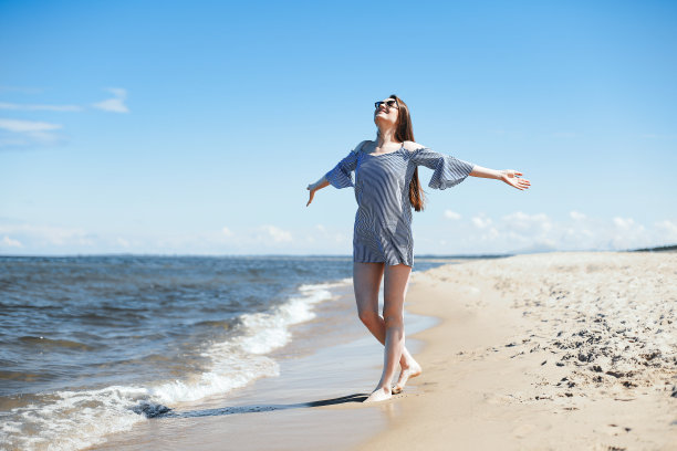 快乐的微笑女人在自由的幸福在海滩上站着张开双手。肖像的黑发女模特在夏季连衣裙享受自然旅行假期假期户外，总体计划图片下载