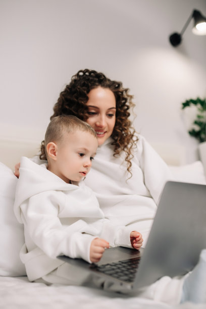 快乐年轻的欧洲母亲和可爱的学龄前儿子使用笔记本电脑，看着电脑屏幕，享受社交媒体聊天，网上购物。一家人在家里一起放松图片下载
