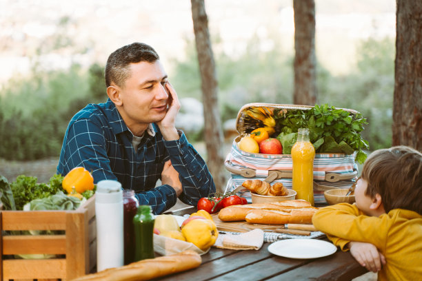 爸爸爸爸和孩子在森林露营地野餐，有蔬菜、果汁、咖啡和羊角面包。木箱新鲜有机蔬菜周围面包法棍。图片下载