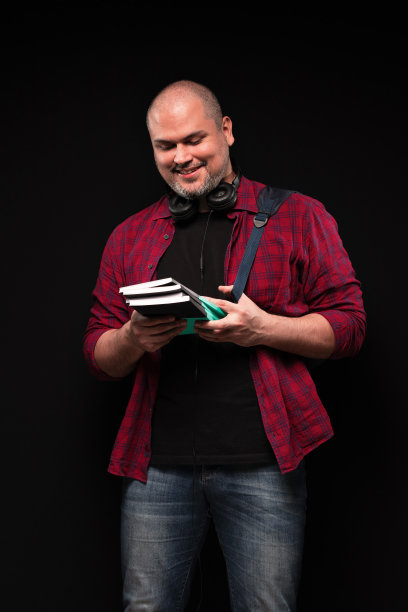 一个巴西男人的肖像，背着背包，戴着耳机，看着手里的书，微笑着，穿着红色纽扣衬衫和蓝色牛仔裤-彩色照片-巴西图片下载