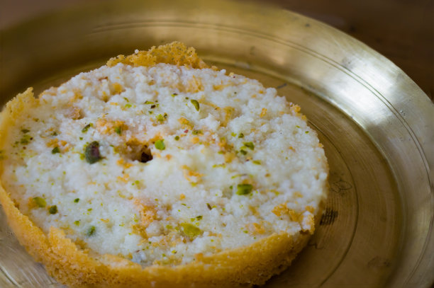 Ghewar或ghevar是拉贾斯坦邦的传统甜点。它是由牛奶、面粉、酥油和糖制成的。上面是干果和马来奶油。这是盛在黄铜盘子里的。照片以复制空间拍摄。图片下载