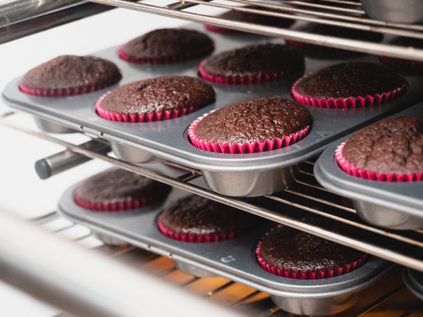 糕点师在专业通风烤箱中烘焙大群黑巧克力纸杯蛋糕图片下载