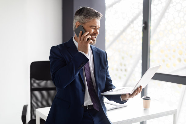 中年商人在办公室打电话和使用笔记本电脑图片下载