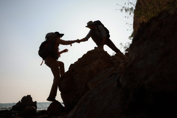 徒步队员手牵手，互相帮助，同时爬上岩石山的冒险旅行概念图片下载