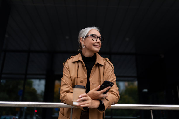 一位年长的成熟女性拿着咖啡在打电话，她看着外面的远方图片下载