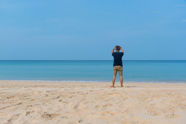 一位年长的成年男子在海滩上拍照。图片下载