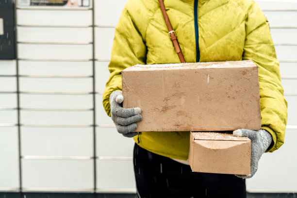 在自助邮件终端机旁，一个女人手里拿着一个盒子。包裹投递机。拿着纸板箱的人。邮件递送和邮政服务，网上购物，电子商务概念图片下载