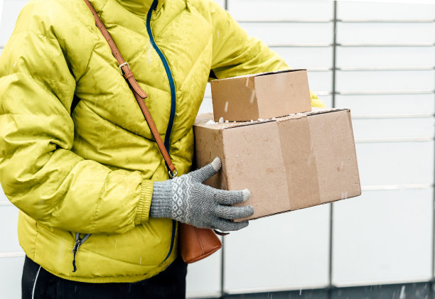 在自助邮件终端机旁，一个女人手里拿着一个盒子。包裹投递机。拿着纸板箱的人。邮件递送和邮政服务，网上购物，电子商务概念图片下载