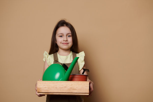 美丽的5岁可爱的女婴对着镜头微笑，带着一个装有园艺工具和浇水罐的木箱图片下载