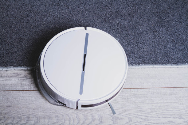 一个白色的真空吸尘器机器人收集灰尘并清洗地板。自动地板清洁。纯洁的概念。从上面看。图片下载